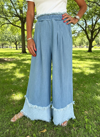 Person wearing light blue denim pants with frayed hem in a sunny park.